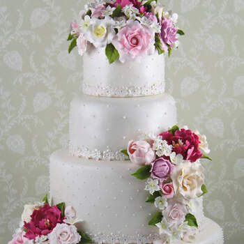 Una tarta romántica y clásica que reproduce en azúcar las flores del ramo de la novia rosas peonías tulipanes y jazmines cubierta de perlas y detalle de encaje en azúcar.