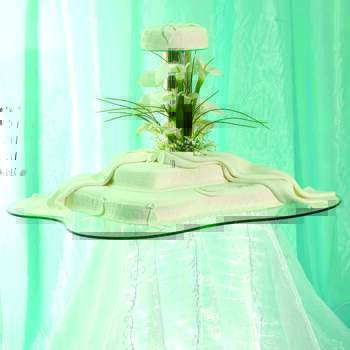 Tarta nupcial de diseño en tres pisos decorada con flores y sobre mesa con velo iluminada