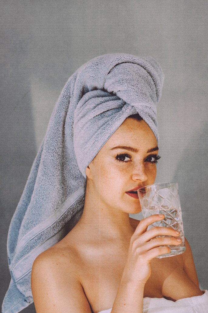 Kobieta ze szklanką wody z ręcznikiem na głowie