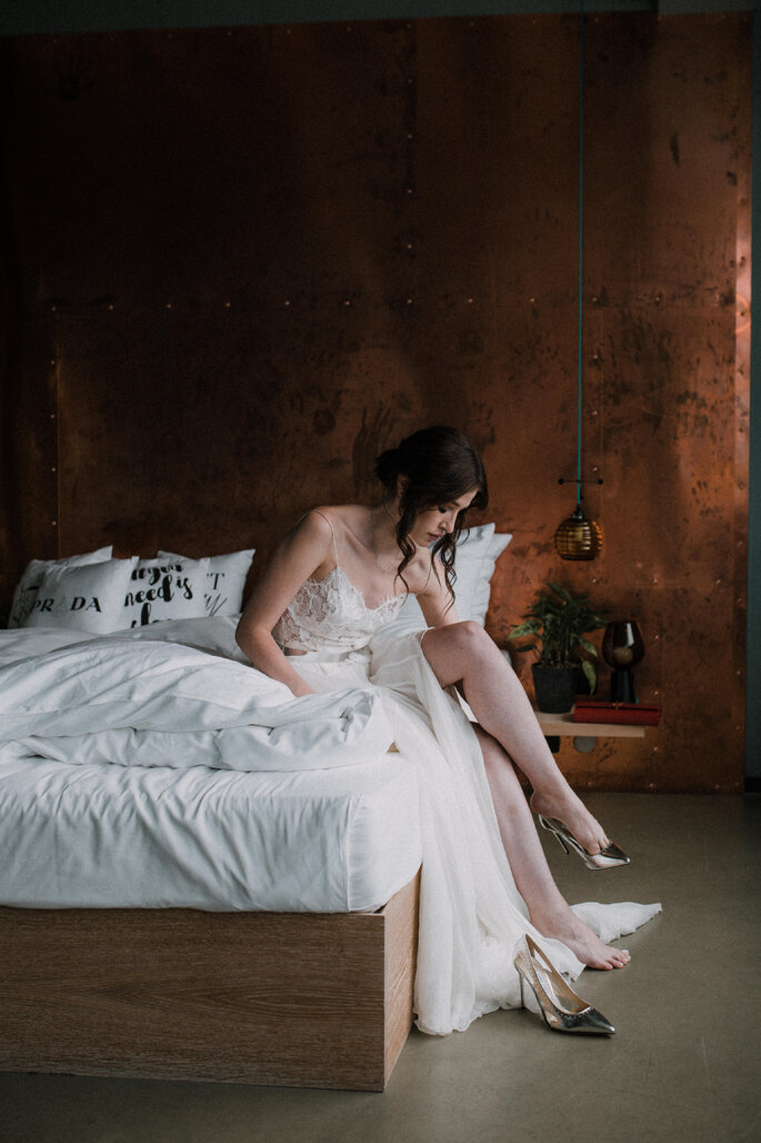 Die Braut sitzt auf dem Bett und zieht ihre Hochzeitsschuhe an.