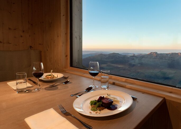 Zwei Teller stehen auf einem Tisch neben einem Fenster. Draußen ist die Alpenkette zu sehen.