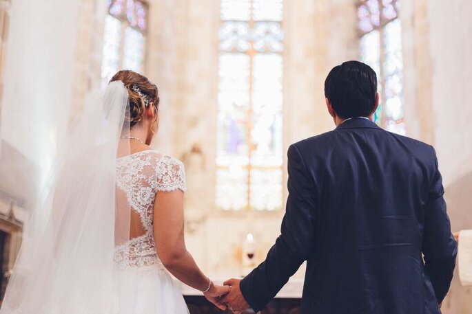 les mariés de dos se tiennent la main dans l'église