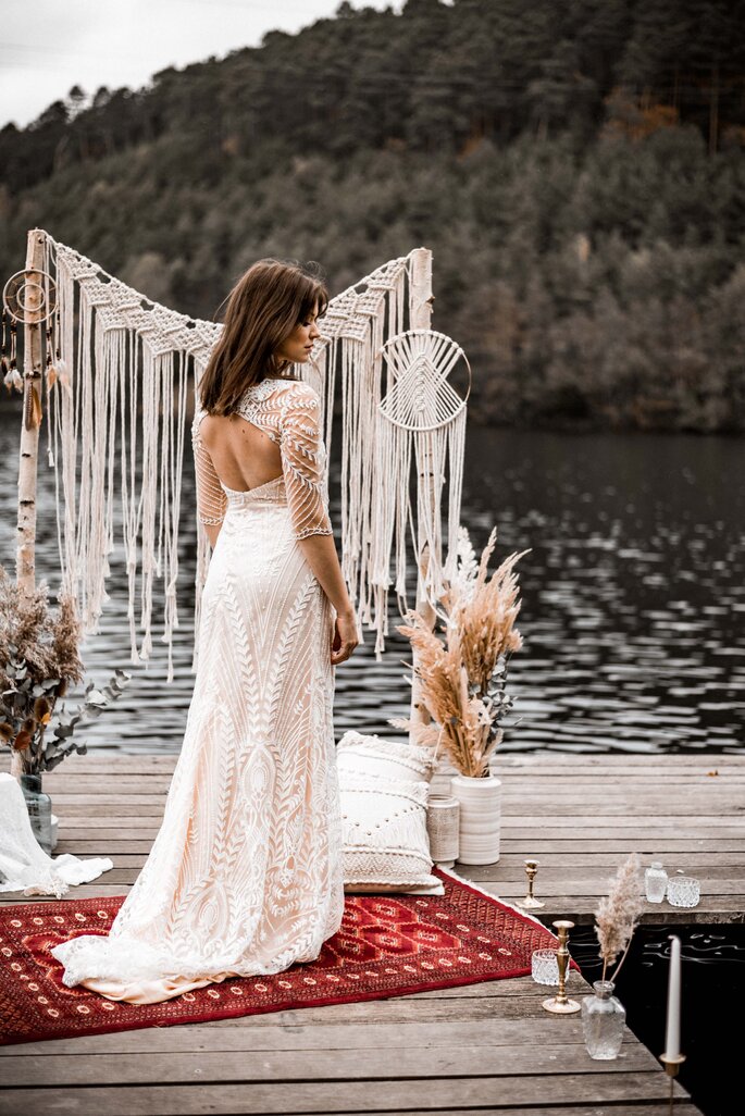 Eine Braut auf einem Bootssteg. Sie trägt ein bodenlanges Brautkleid mit tiefem Rückenausschnitt.