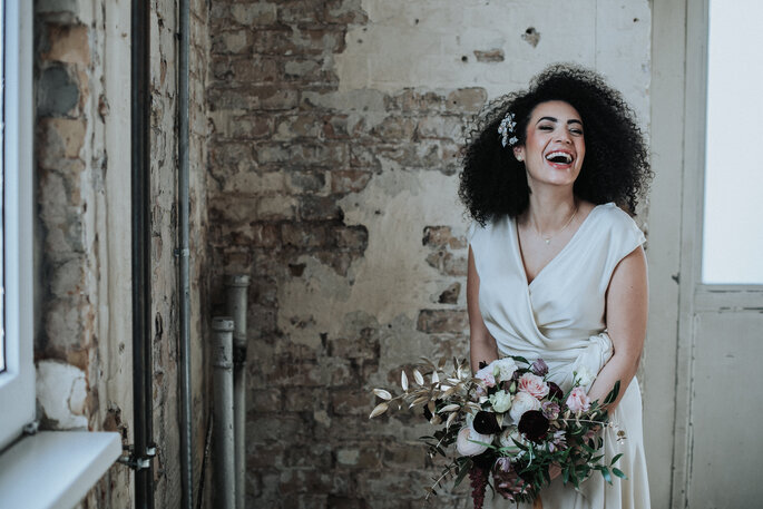 Porträt der lachenden Braut im weißen Kleid mit Brautstrauß, organisiert von Freakin' Fine Weddings.