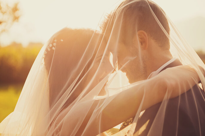 Hochzeitsfoto. Brautpaar schaut sich in die Augen vor Sonnenuntergang, verdeckt vom Schleier der Braut