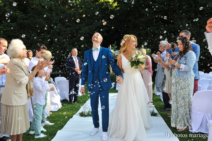 Deux mariés marchent dans l'allée sous les bulles et applaudissements de leurs invités 