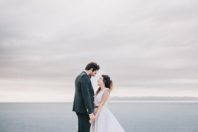  Deux mariés en train de se tenir les mains et de se regarder devant l'océan
