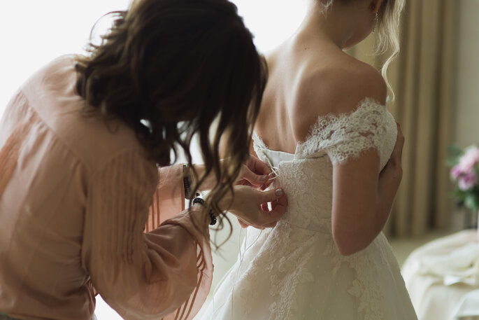 Madrinha ajuda a noiva a amarrar o vestido