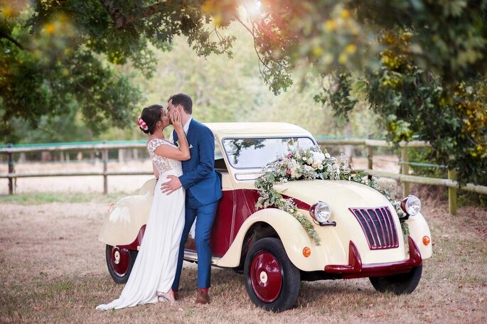 Des mariés s'embrassent devant une voiture de collection décorée pour leur mariage - EC-Photographie