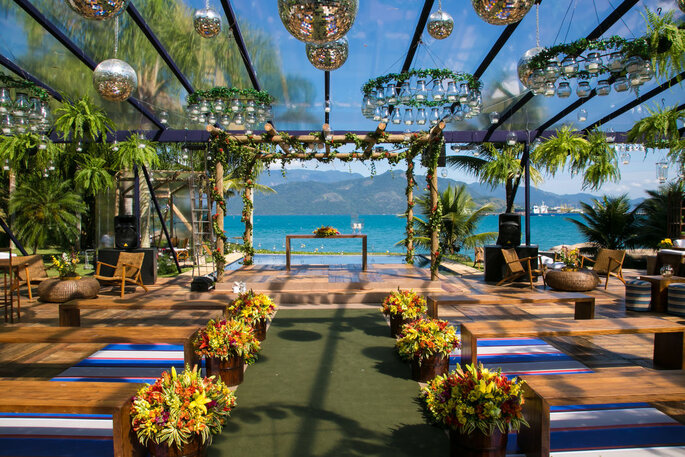 Casamento em frente a praia, com cobertura, tapete verde e flores coloridas