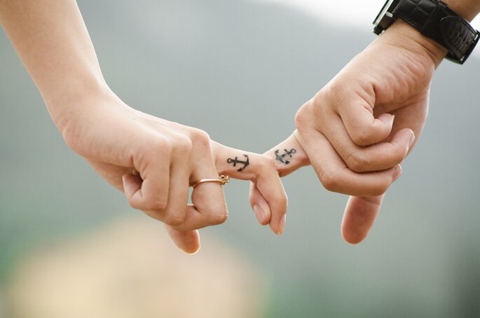 Couple se tenant la main. Les deux ont le même tatouage sur le doigt qui représente une ancre. 