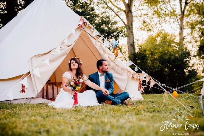 Un couple de mariés assis à l'entrée de sa tente tipi Mon Wedding Camping