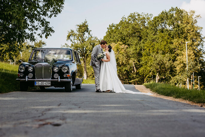 Das Brautpaar beim Shooting mit Hochzeitsauto, Foto von Hüttner Fotografie.