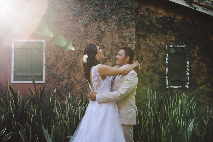 Casal em casa, se abraçando em frente ao muro de folhas com janelas