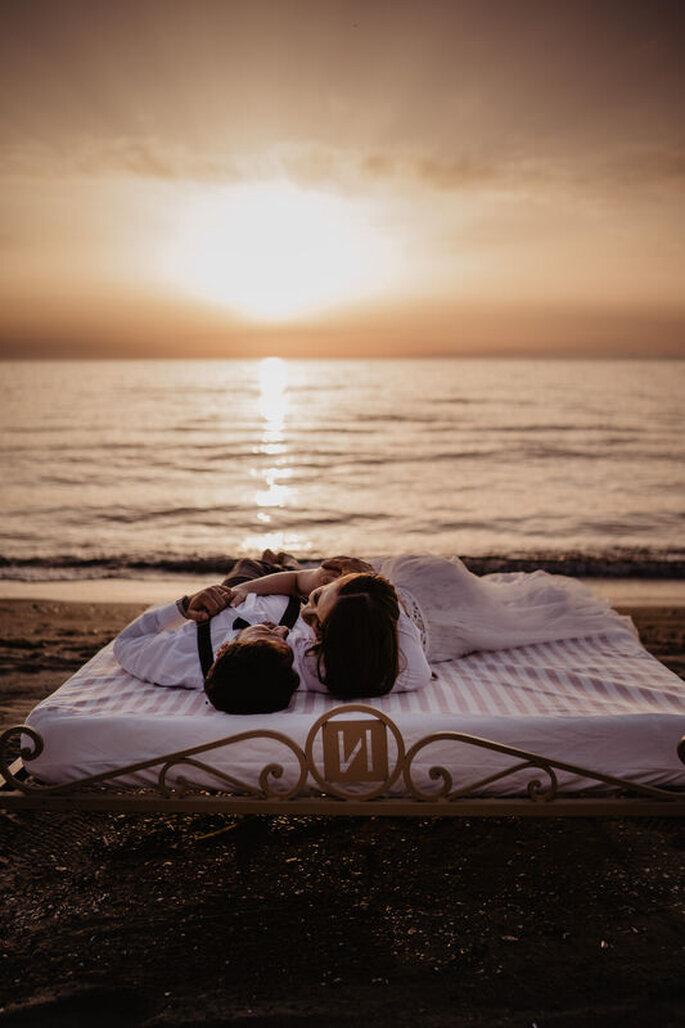 sposi su un letto in riva la mare, tramonto