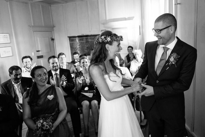 Ein Brautpaar hält sich bei der Trauung an den Händen und lacht.