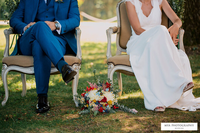 Des mariés assis sur de jolies chaises pendant leur cérémonie laïque, le bouquet de la mariée à leurs pieds.