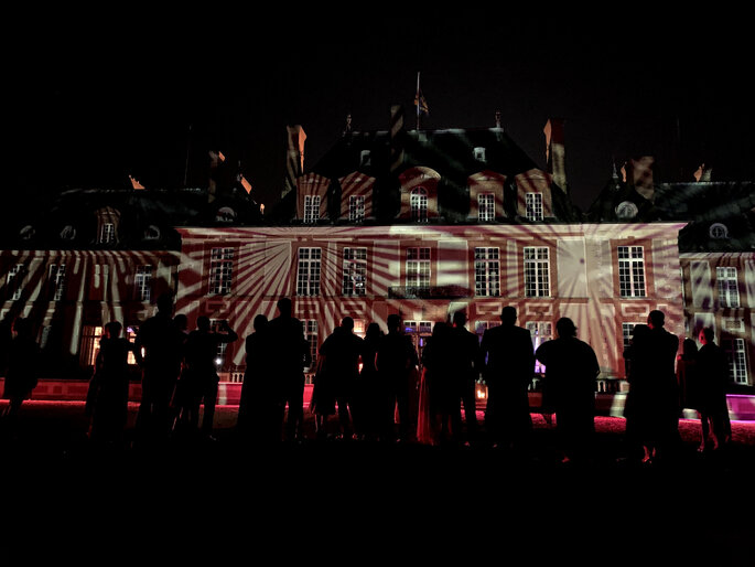 Les invités d'un mariage contemplent une façade illuminée grâce à des jeux de lumière originaux