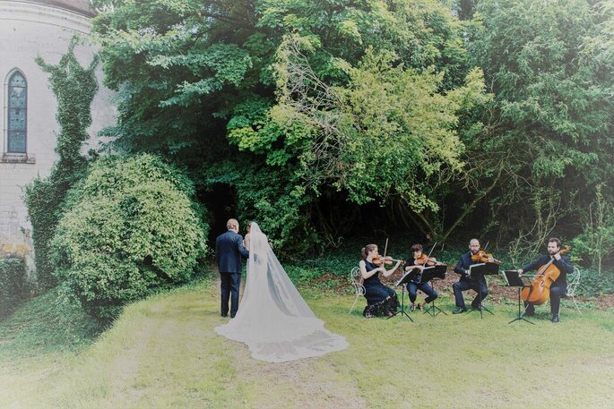Une mariée accompagnée par son père au son d'instruments à cordes