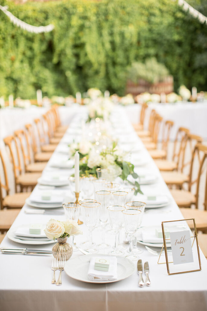 Table dressée pour un mariage champêtre avec des chaises en bois, des bouquets de fleurs blanches, des couverts en argent et des assiettes blanche