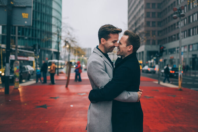 Zwei Männer liegen sich lachend vor einer Stadtkulisse in den Armen.