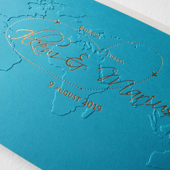 Faire-part de mariage bleu avec la map monde gravée en relief et les noms des mariés en doré