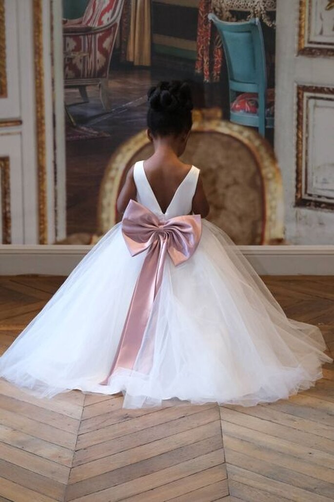 Une petite fille d'un cortège de mariage en robe blanche agrémentée d'un nœud rose