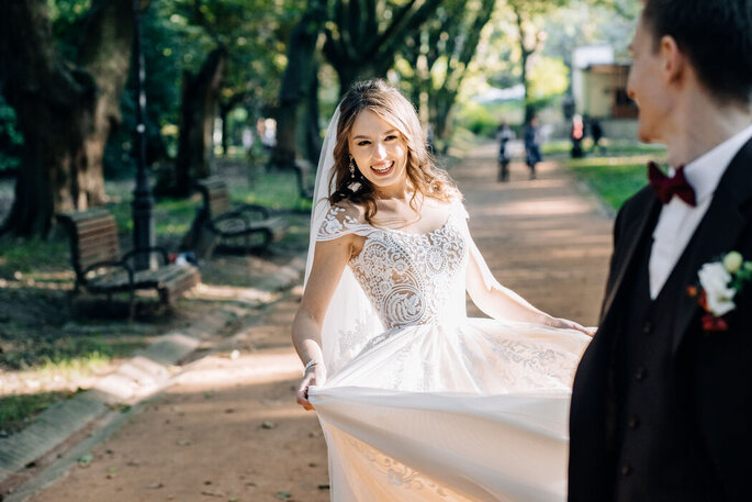 Eine Braut lacht im Park in eine Kamera.