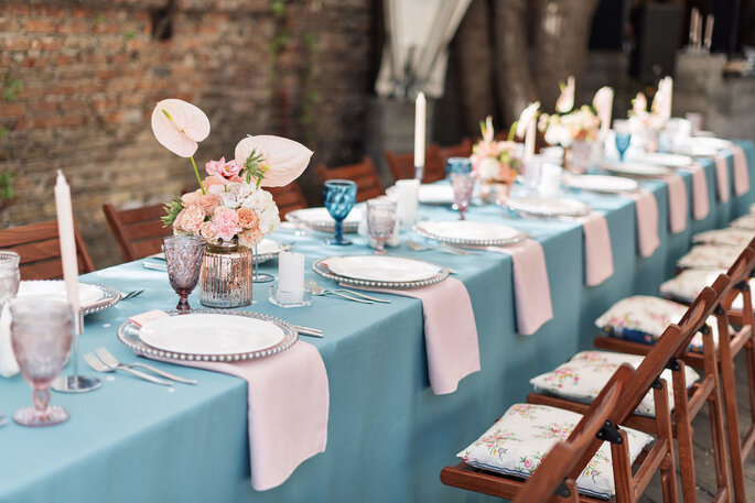 Table de mariage décorée avec une nappe bleu, des serviettes roses et des bouquets de fleurs 