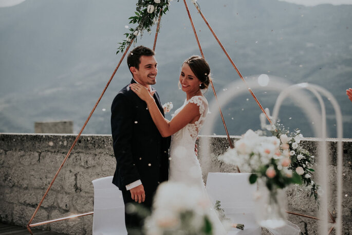 Ma petite cérémonie - Deux mariés dans un instant de complicité sous une arche tipi fleurie, face aux montagnes 