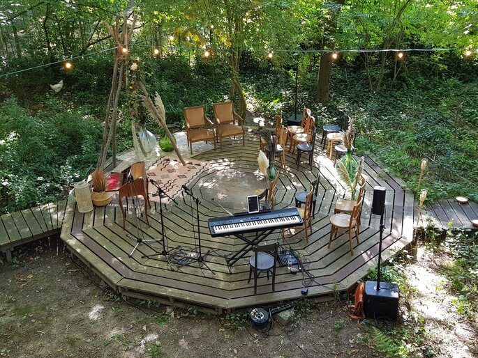 une esplanade en bois au milieu de la foret avec des chaises et un piano 