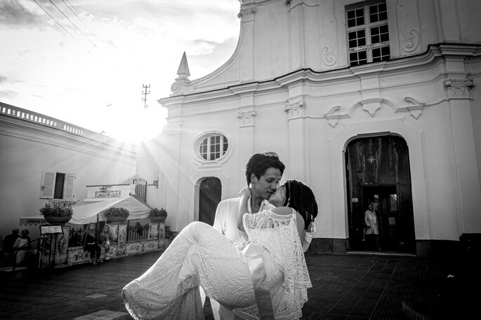 sposa in braccio allo sposo fuori dalla chiesa, i raggi del sole fanno capolino