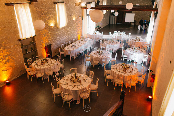 Salle de réception aménagée pour un mariage, avec des tables décorées et des murs de pierres apparentes