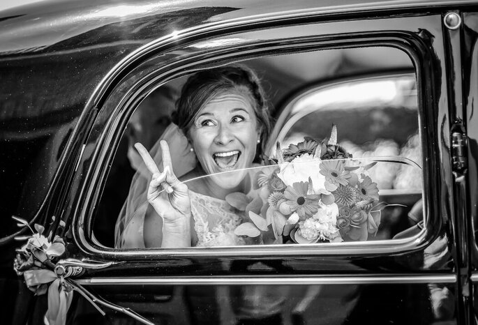 photo en noir et blanc d'une mariée qui tient un bouquet de fleurs, assise dans une voiture 