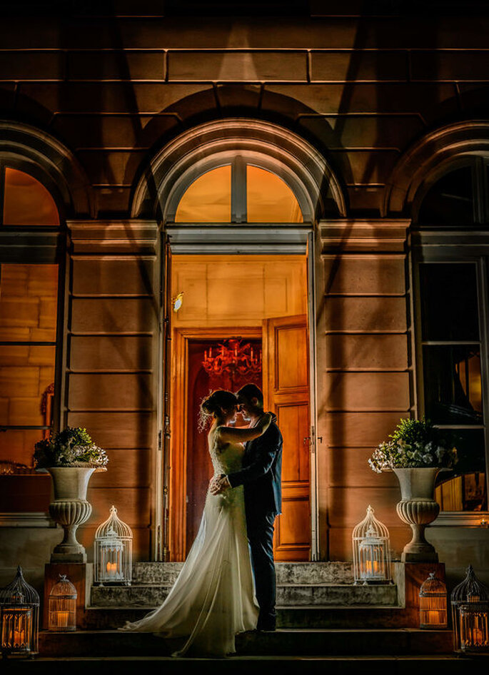 deux mariés sur des escalier en pierre devant l'entrée d'une salle de réception 