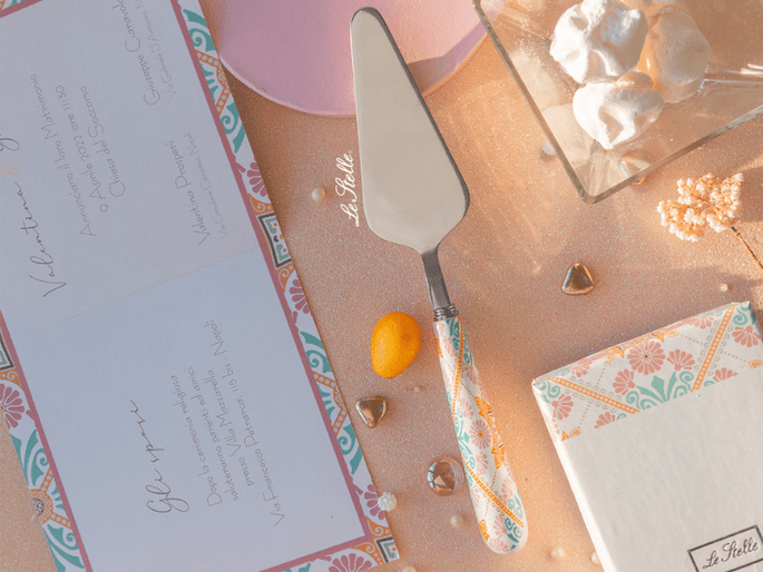 paletta per torta con manico decorato, su tavolo tra invito in pendant e confetti 