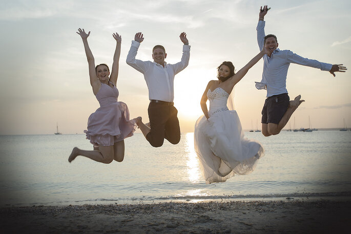 Ein Brautpaar und ihre Gäste springen am Strand in die Luft.