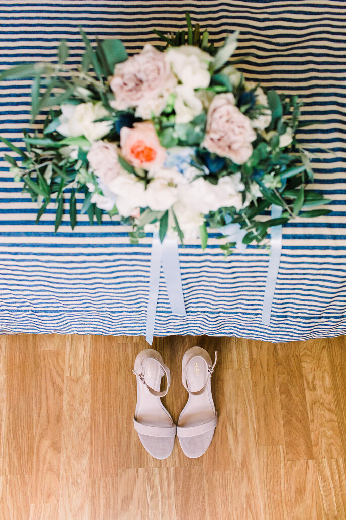 bouquet de noiva em cima de uma toalha de riscas com os sapatos de noiva em baixo