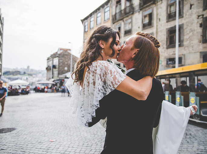 casal de noivos noiva ao colo beijarem-se na rua