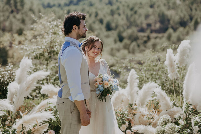 Pareja de novios en el campo con ramo de novia en colores beige y azul