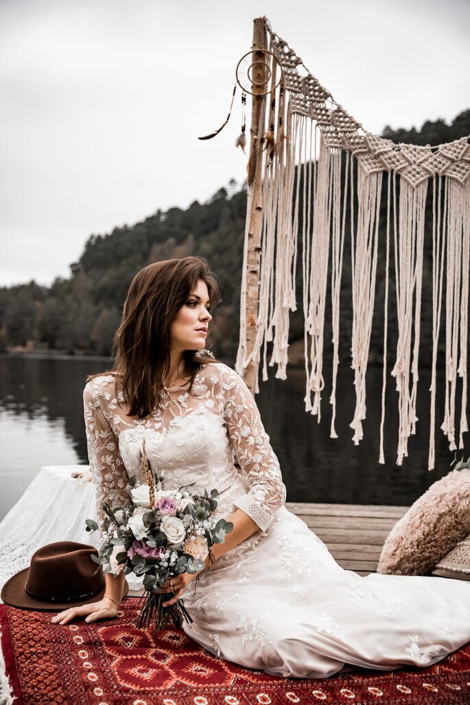 Eine Braut sitzt auf einem Bootssteg und hält einen Brautstrauß in der Hand.